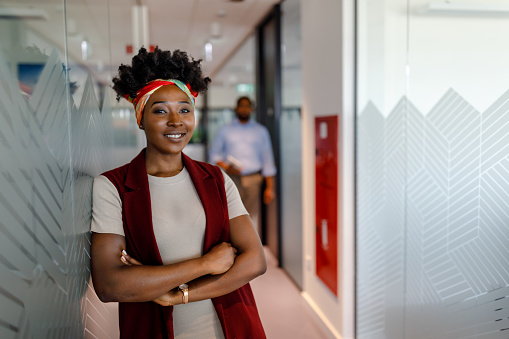 Photo of a Young Business Woman of African-American Ethnicity in the Hallway of a Company Feeling Confident and Satisfied.