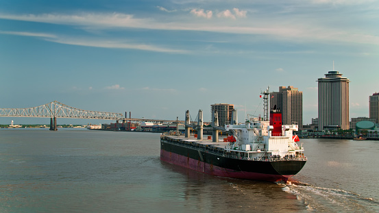 Drone shot of a bulk carrier on the Mississippi River in New Orleans, following the ship as it travels up the Mississippi past the central business district towards the Crescent City Connection Bridge.