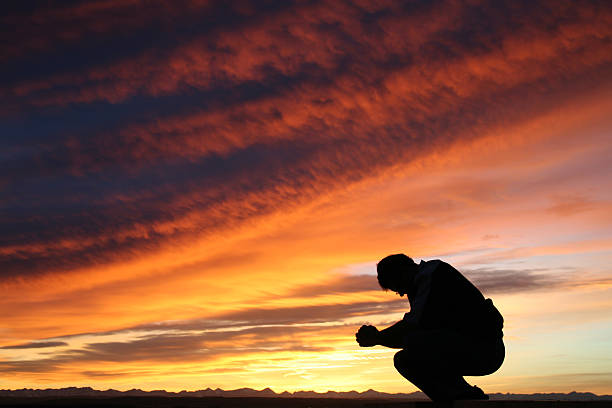 nicht erkennbare kaukasischen männer beten vor dramatischen sonnenuntergang-himmel - praying men god kneeling stock-fotos und bilder
