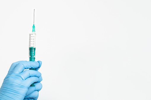 A doctor's hand in a medical glove holds a syringe with a needle to protect against the flu virus. Cvd vaccine. The concept of medicine vaccination treatment with subcutaneous injections, copy space.