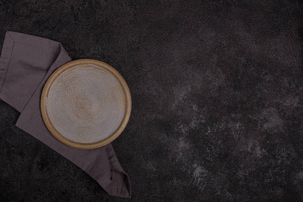 istock An empty beige ceramic plate on a dark black background. Grey linen napkin. 1340628205