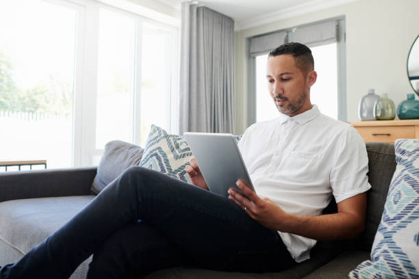 istock Shot of a young man sitting on his sofa at home and using a digital tablet to work from home 1340636165