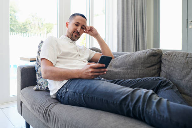 istock Shot of a handsome young man sitting on his sofa at home and looking contemplative while using his cellphone 1340636177