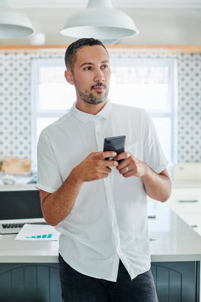 istock Shot of a handsome young man standing alone in his kitchen and looking contemplative while using his cellphone 1340636204