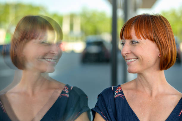 Amused joyful woman looking at her own reflection in a large commercial plate glass window in a quiet city street with a happy smile in a close up portrait