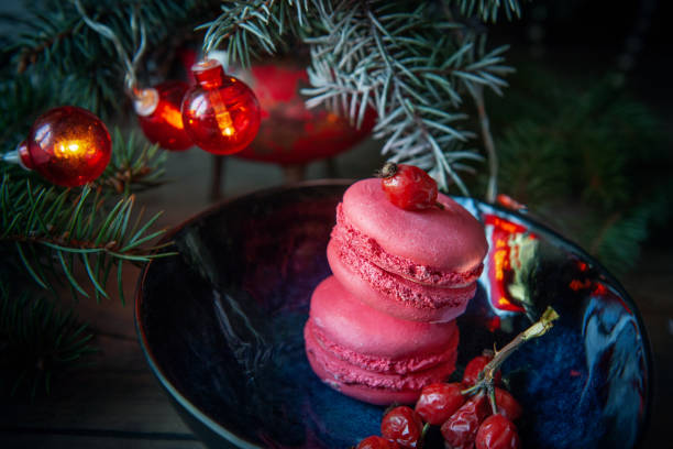 istock Two raspberry macaroons lie on a plate on the table in front of a Christmas tree garland and a branch of red ripe rose hips. Christmas composition 1340640313