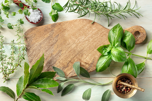 Cooking with herbs. A wooden cutting board with salt, pepper and aromatic herbs. Basil, bay leaf, rosemary, thyme, sage, oregano, and lemon balm