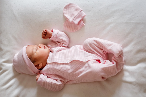 Cute little newborn baby girl of one week sleeps sweetly on a white blanket in natural light