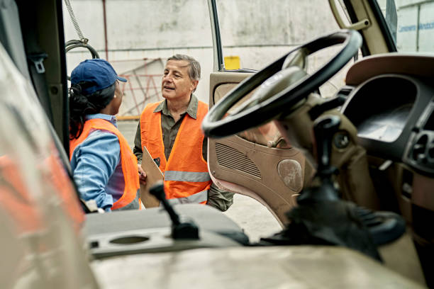 Truck Driver Communicating with Worker at Loading Dock Personal perspective from inside vehicle cab of mid 20s Black woman talking with early 60s Caucasian man holding clipboard before beginning road trip. passenger cabin photos stock pictures, royalty-free photos & images