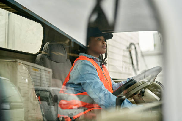 Black Female Truck Driver Photographed Through Window Personal perspective of mid 20s woman in casual clothing, cap, and reflective vest sitting in driver’s seat, looking straight ahead, ready to begin road trip. passenger cabin photos stock pictures, royalty-free photos & images