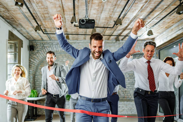 Large group of cheerful entrepreneurs having a sports race in the office. Large group of cheerful business people crossing the finish line during sports race in the office. race office stock pictures, royalty-free photos & images