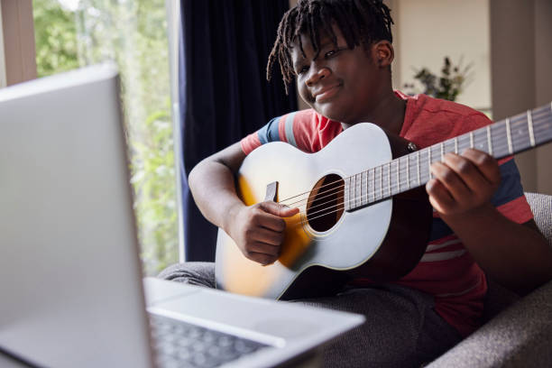십대 소년 집에서 노트북 컴퓨터에 온라인 수업과 수의 기타를 재생하는 학습 - guitar child music learning 뉴스 사진 이미지