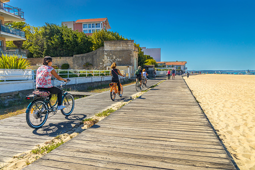 Tourists on bikes on a wooden cycle path on a beach in Arcachon on a summer day in France