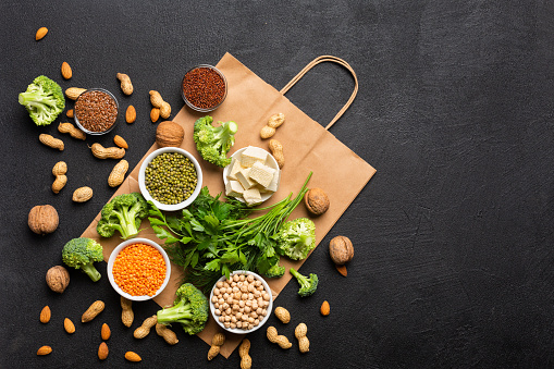 Concept: Purchase healthy clean food. Protein source for vegetarians: vegetables, nuts, seeds  and legumes top view on a black background with a paper bag.