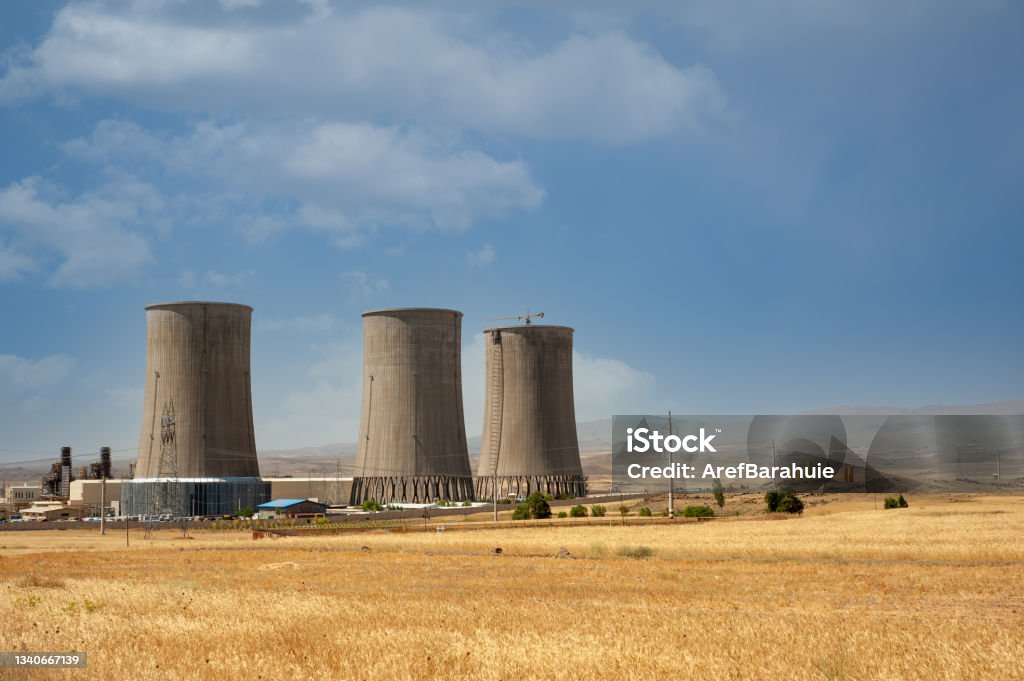 Nuclear power plant cooling towers, big chimneys beside Wheat field with partly cloudy sky in Kurdistan province, iran Nuclear Power Station Stock Photo