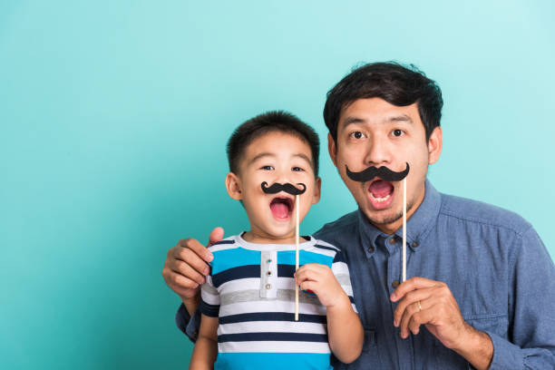 Family funny happy hipster father and his son kid holding black mustache props stock photo