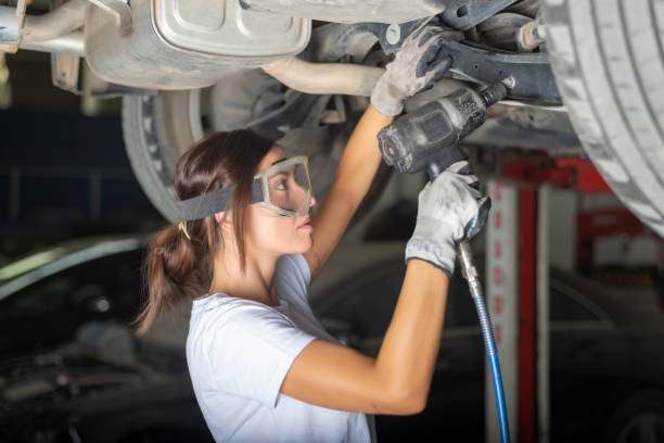 A young woman fixing the underbody of a car with a  impact wrench in a garage. stock photo