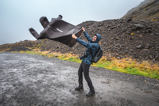 Man holding his rain poncho against strong wind in Iceland.