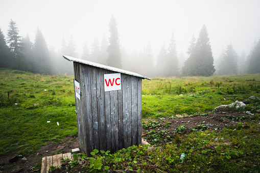 A small wooden toilet structure outdoors in mountain wilderness.