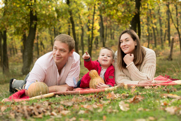 Fall. Close-up of happy family on the background of the autumn forest. Happy mom, dad and son are smiling. Fall. Close-up of happy family on the background of the autumn forest. Happy mom, dad and son are smiling. women lying down grass wood stock pictures, royalty-free photos & images