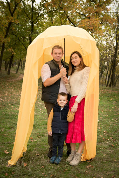 Fall. Portrait of happy mom, dad and son under an umbrella with a yellow veil. Fall. Portrait of happy mom, dad and son under an umbrella with a yellow veil. women lying down grass wood stock pictures, royalty-free photos & images