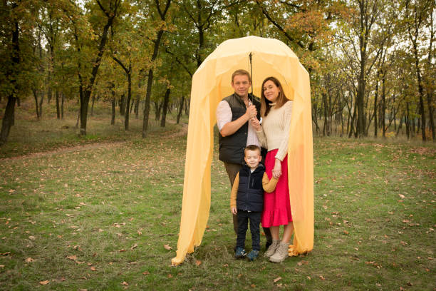 Fall. Portrait of happy mom, dad and son under an umbrella with a yellow veil. Fall. Portrait of happy mom, dad and son under an umbrella with a yellow veil. women lying down grass wood stock pictures, royalty-free photos & images