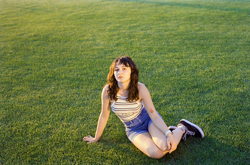 Young Caucasian woman sitting on lawn at sunset. Camera film photo