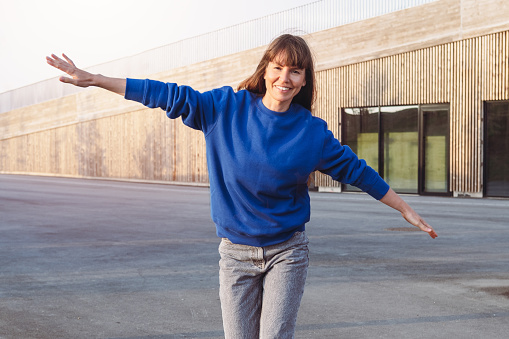Smiling cheerful brunette woman running with outstretched arms. Woman wears blue sweatshirt.