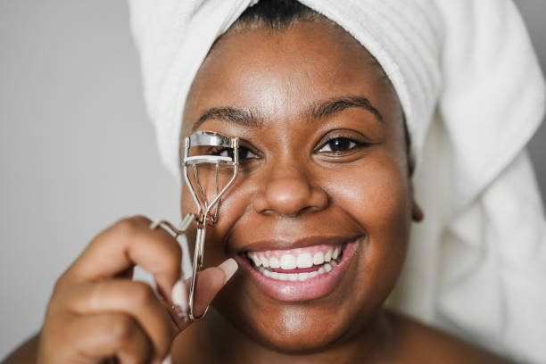istock Black girl using eyelash curler while wearing body towel - Main focus on eyes 1340684240