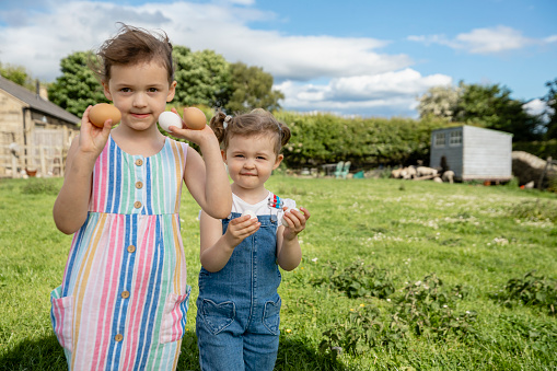 A close-up portrait shot of two young girls, they are at their parent's farm in North East, England. They are holding up chicken eggs they have collected at the farm.