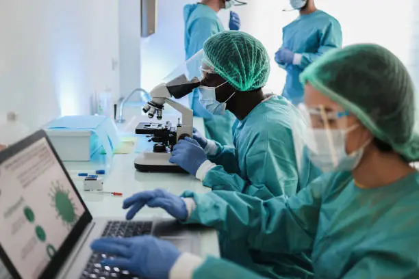 Medical doctor working with microscope and laptop computer inside hospital lab - Focus african man face