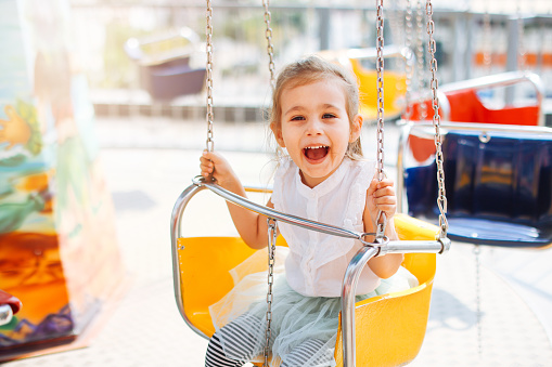 Cute little girl enjoing time at fun fair, chain swing ride, amusement park in summer