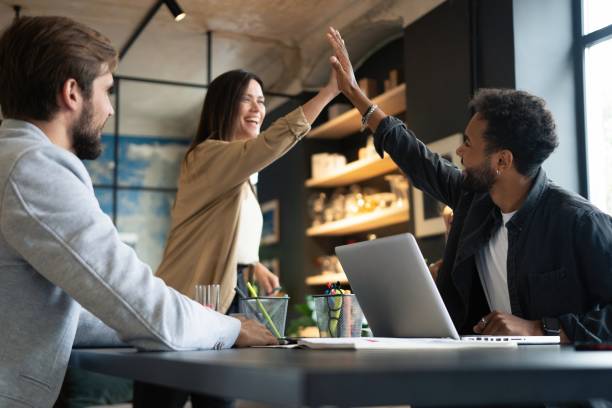 istock Two cheerful young business people giving high-five while their colleagues looking at them and smiling. 1340692191