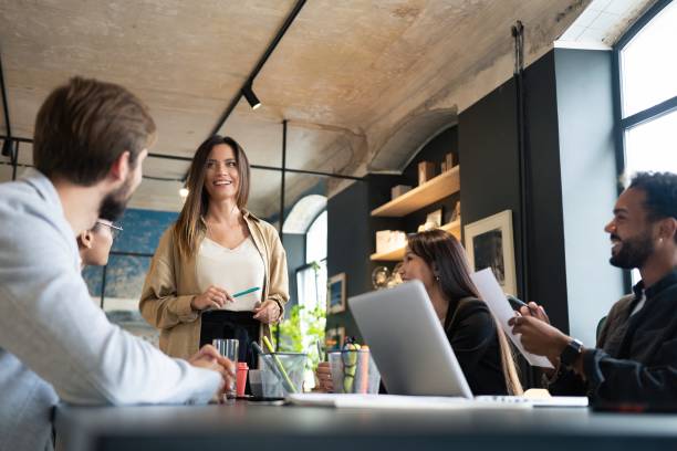 líder ejecutiva hablando con un grupo de empleados diversos y felices en la sesión informativa de la oficina corporativa - entrenar fotografías e imágenes de stock