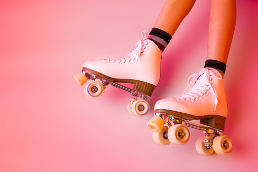 Retro classic white leather roller skates and girlâs legs - sports equipment and recreation. Pastel pink background. Layout with free copy (text) space.