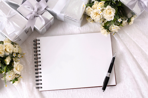 Wedding album or writing book laid on bridal lace with several silver wedding gifts and white rose bouquets.  Alternative version of this file shown below: