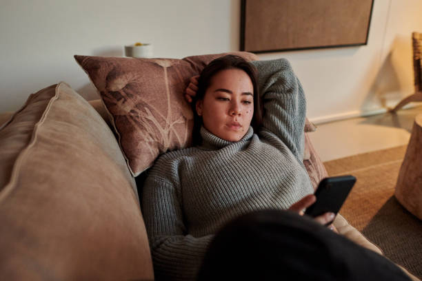 istock Shot of a young woman relaxing on her sofa using her smartphone to send text messages 1340696949