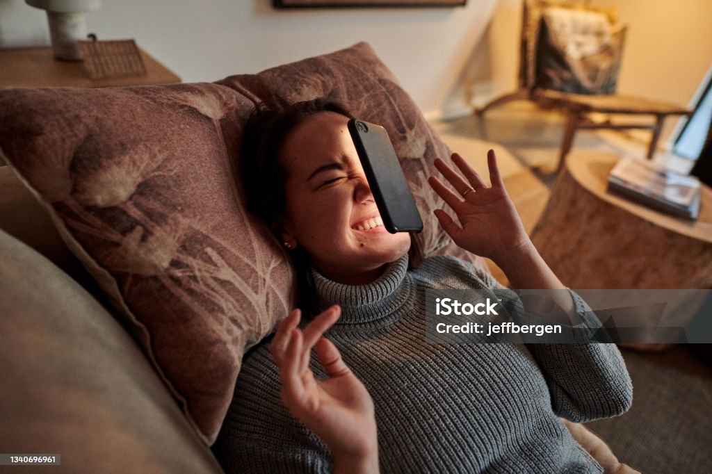 Shot of a young woman lying on the couch after her phone fell on her face Slippery hands are never a good thing Falling Stock Photo