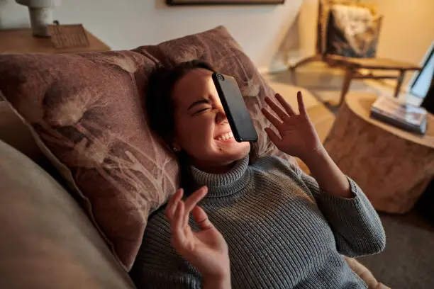 Photo of Shot of a young woman lying on the couch after her phone fell on her face