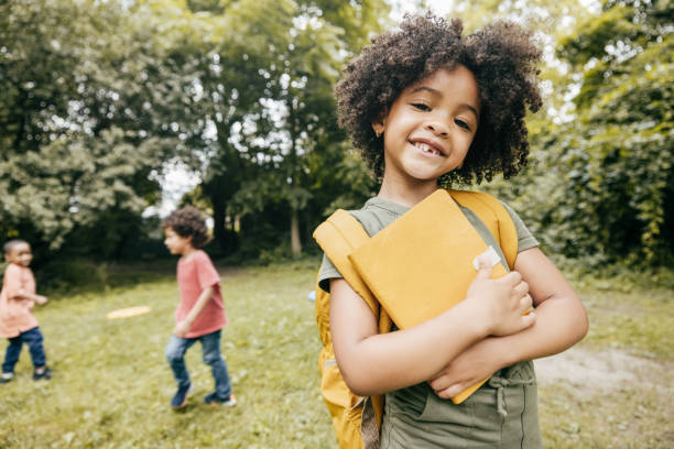 Maximizing Learning and Engaging Students Shot of cute elementary school girl smiling and looking at camera meanwhile her school friends are in the background. first day of school stock pictures, royalty-free photos & images