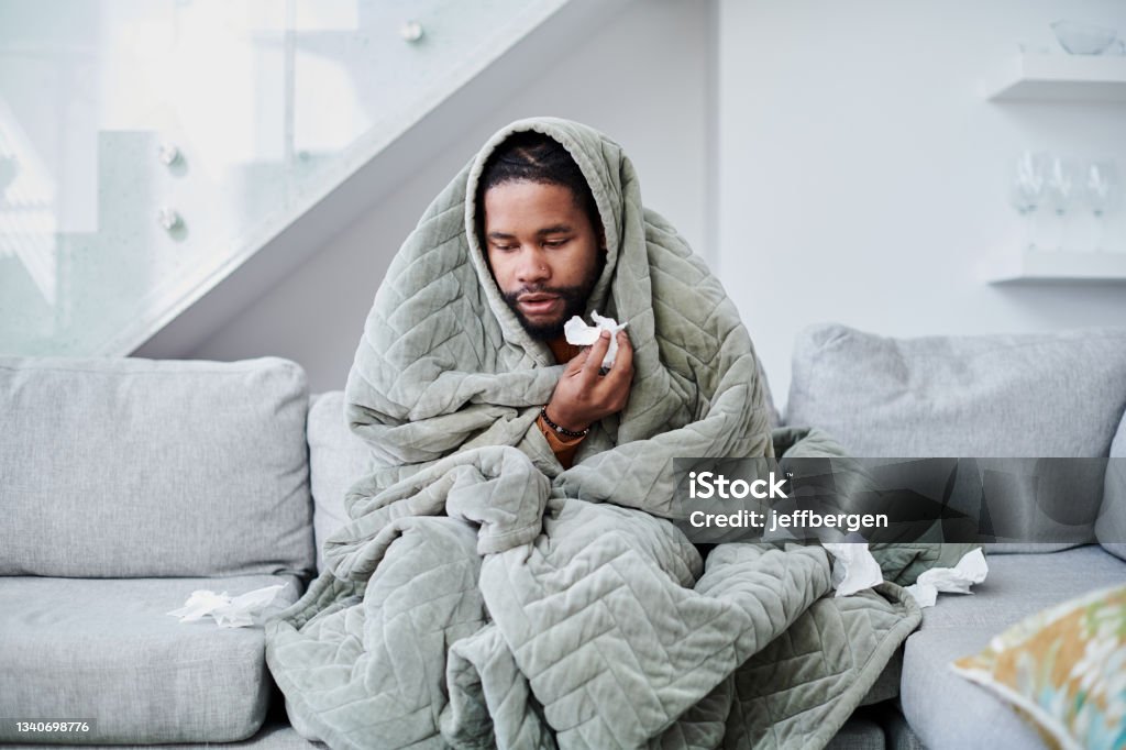 Shot of a young man with the flu sitting on the couch at home If you be sick, your own thoughts make you sick Illness Stock Photo