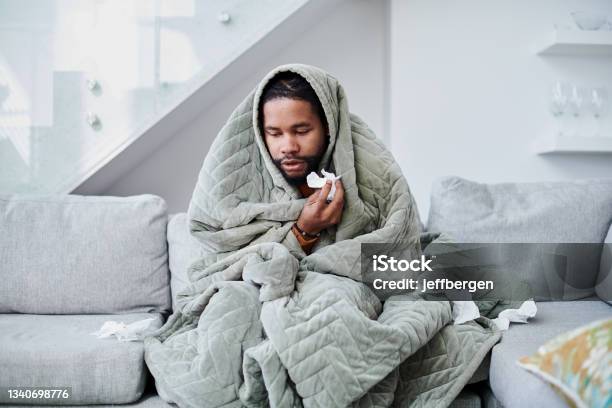 Shot Of A Young Man With The Flu Sitting On The Couch At Home Stock Photo - Download Image Now