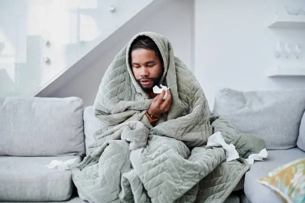 Photo of Shot of a young man with the flu sitting on the couch at home