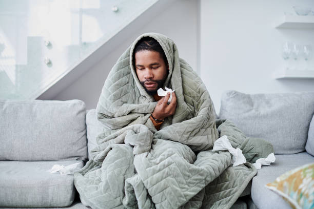 снимок молодого человека с гриппом, сидящего дома на диване - болезнь стоковые фото и изображения