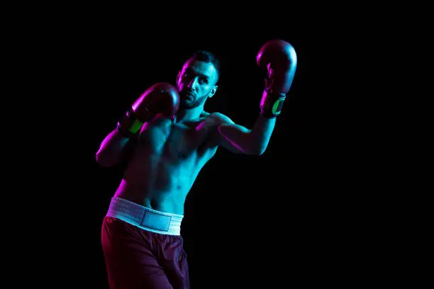 Photo of Portrait of one professional boxer training isolated over black background in neon light.