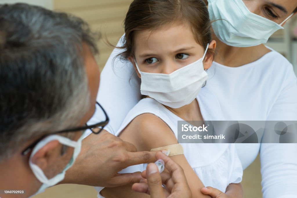 Vaccination Child with protective face mask is sitting in her mothers lap and  is getting vaccination from a doctor. Hepatitis Stock Photo