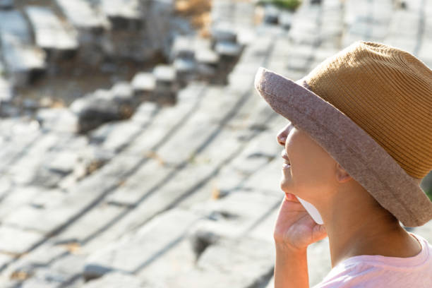 Side view of an unrecognizable caucasian female tourist who is using her phone  in an ancient amphitheater. Steps of the amphitheater are visible in the background.