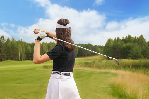 selective focus of smiling female golf player in cap with golf gear at golf course