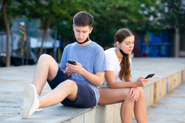 istock Teens in protective masks write messages on smartphone on city street 1340706900