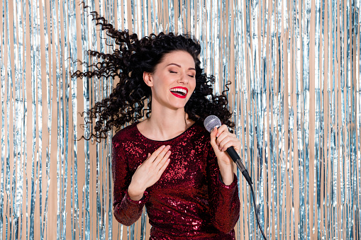 Photo of young pretty lovely happy cheerful smiling girl with flying hair singing in karaoke isolated on shiny background.